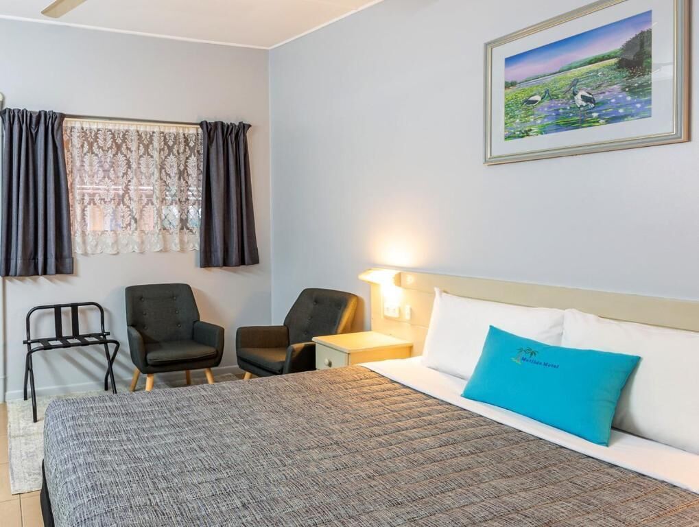 A hotel room with a bed, two chairs, a nightstand, a lamp, and a framed picture on the wall.