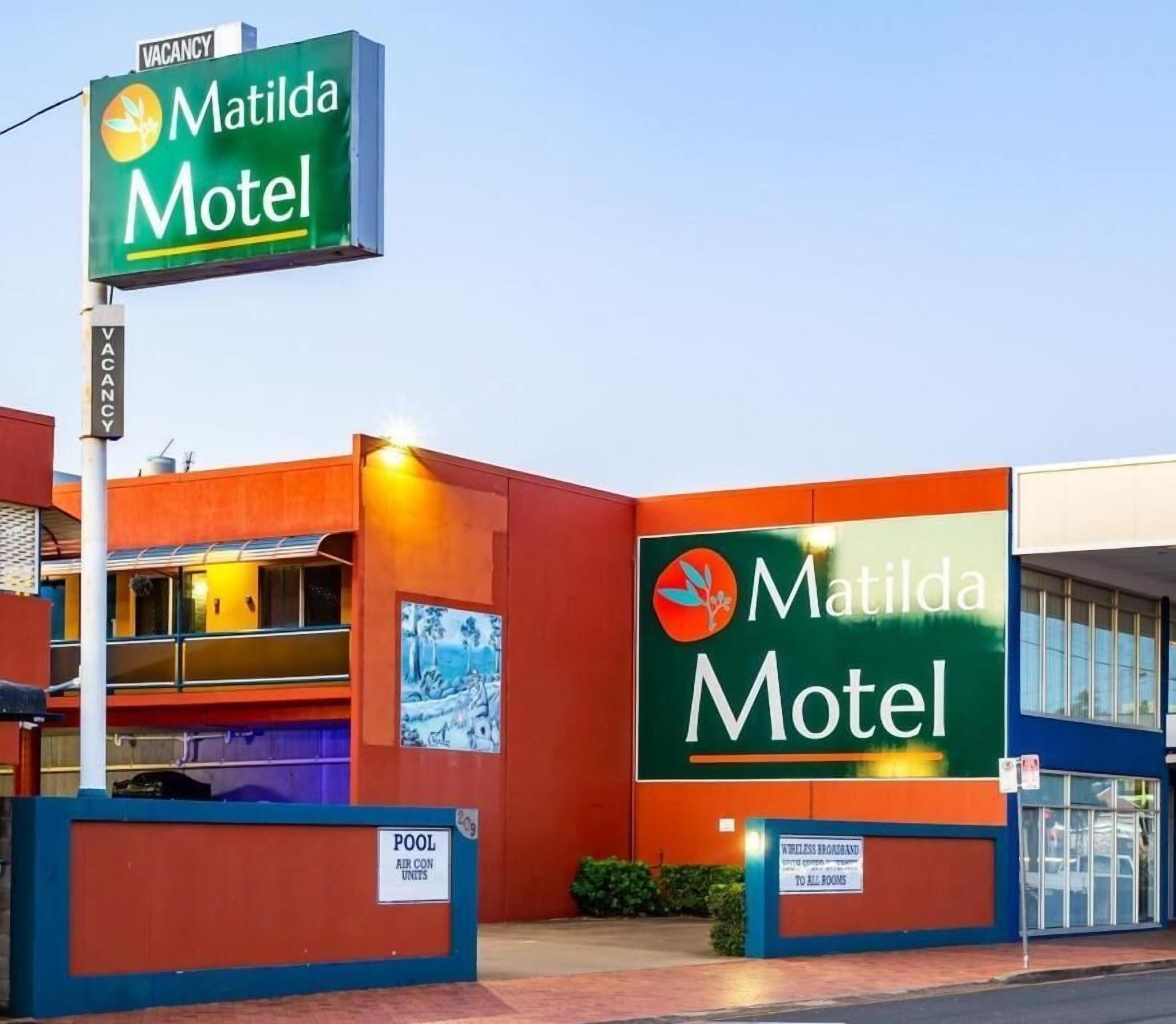 Een motel met een opvallend groen bord, een zwembadgedeelte en een duidelijke ingang.