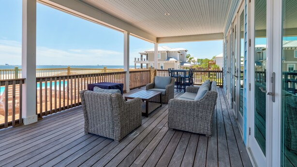 A covered outdoor deck with wicker furniture and a view of the ocean. - Coastal Charm | Nightly stays starting 9/20! Pool (Dauphin Island)