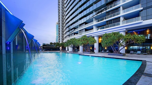 A swimming pool with a modern building in the background. - Converted 2 Bedroom Apartments (No Parking) - WOWSTAY (Surfers Paradise)