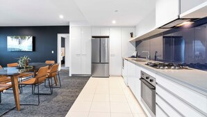 A modern kitchen with white cabinets, a stainless steel refrigerator, and a gas stove. - Converted 2 Bedroom Apartments (No Parking) - WOWSTAY (Surfers Paradise)
