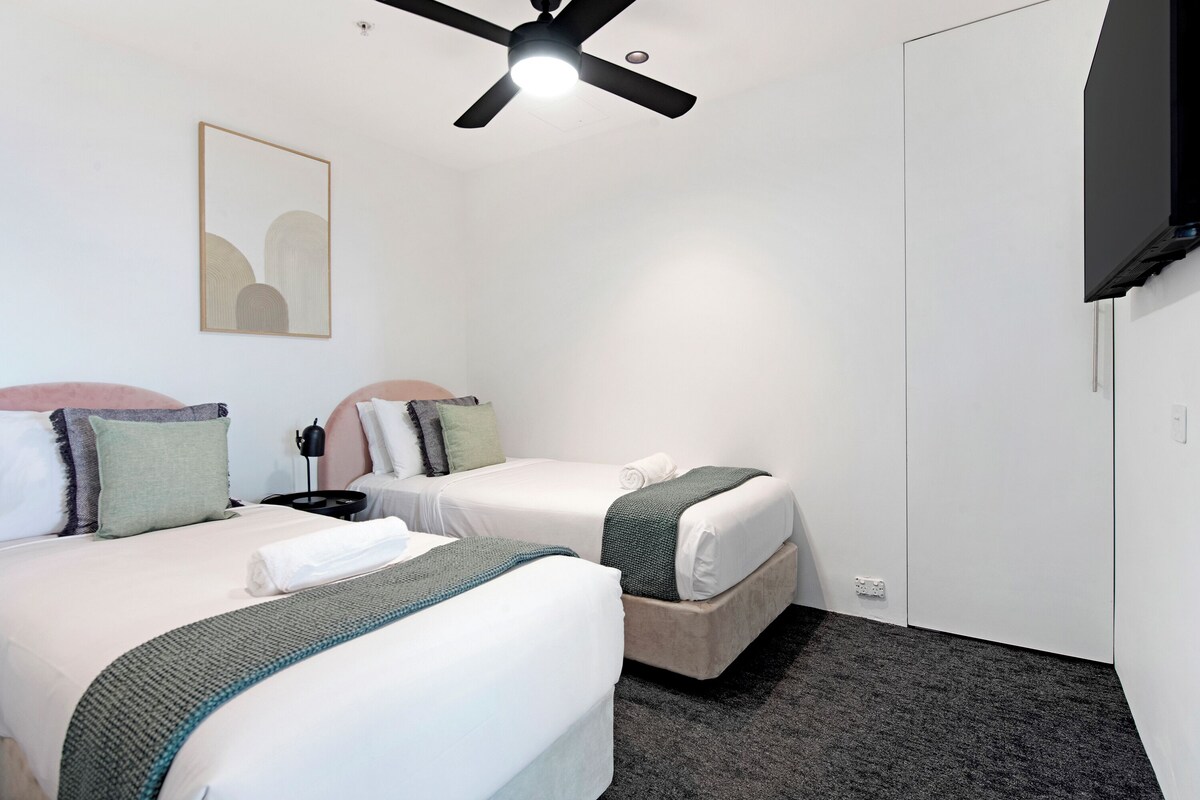 Ein Hotelzimmer mit zwei Betten, einem Deckenventilator, einem Fernseher und einem gerahmten Kunstwerk an der Wand.