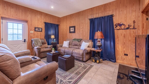 A cozy living room with wooden walls, a large window, and a fireplace.