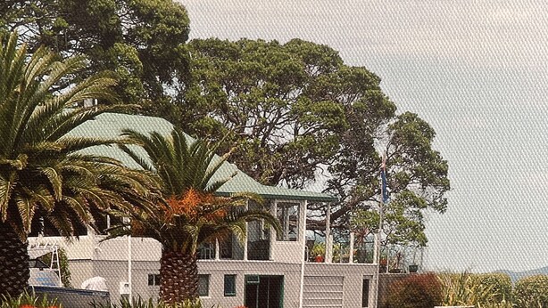 A coastal building with a balcony, surrounded by lush greenery and a rocky shoreline.