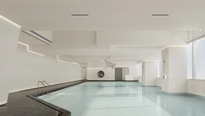 A modern indoor swimming pool with a long, narrow design, surrounded by white walls and minimalistic decor. - Yutai hotel-Style Apartment (Shenzhen)