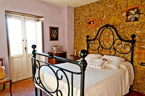 A bedroom with a stone wall, a bed with white linens, a metal headboard, a wooden nightstand, and a door with a view. - Wonderful private villa for 6 guests with WIFI, A/C, private pool, TV, patio and panoramic view (Botinaccio)