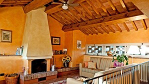 A cozy living room with a fireplace, a sofa, a striped armchair, and a ceiling fan.