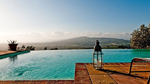 An infinity pool with a clear view of distant mountains, a lantern, and a potted plant.