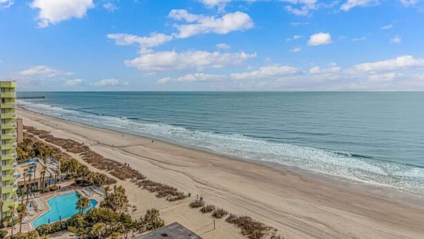 A beach view with a swimming pool, a hotel building, and a clear sky. - Sea Mist 21006 (Myrtle Beach)
