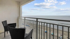 A balcony with wicker furniture overlooking a beach with people and umbrellas. - Sea Mist 21006 (Myrtle Beach)