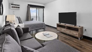 A modern hotel room with a sofa set, a round coffee table, a TV on a wooden stand, and a window with curtains. - Sea Mist 21006 (Myrtle Beach)