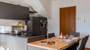 A modern kitchen with a dining area, featuring a built-in oven, microwave, and a wooden dining table set for four. - Cristina by Interhome (Gravedona)