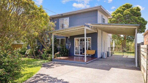 Ein zweistöckiges Haus mit überdachter Terrasse, Holzdeck und umzäunter Garten.