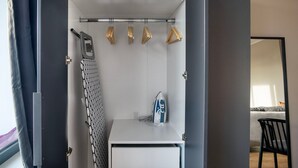 Ein kleines Hotelzimmer mit integriertem Kleiderschrank, einer kompakten Bügeleinrichtung und einem Bett im Hintergrund.
