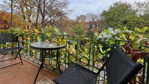 An outdoor patio with a round table and two chairs, surrounded by a green metal fence and foliage. - AAA STAY PREMIUM Old Town Mariensztat (Warsaw)