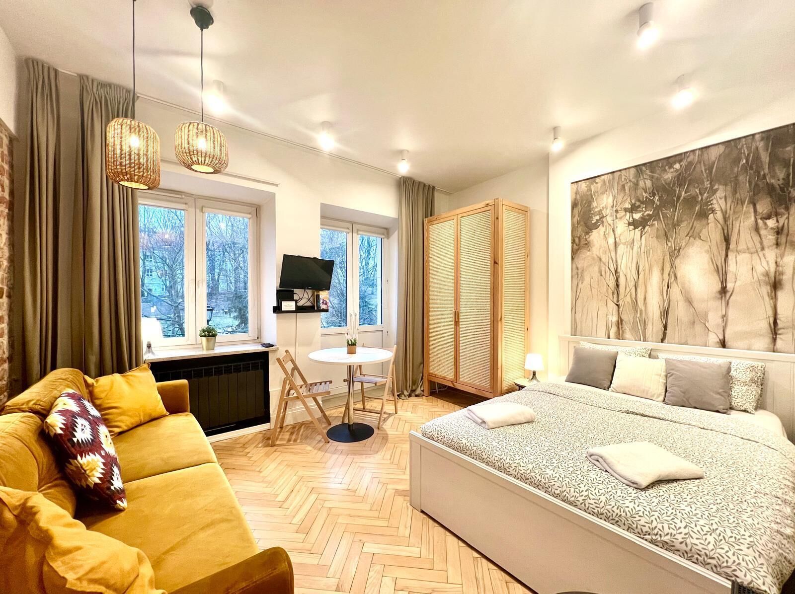 A modern bedroom with a large bed, a sofa, a dining table, and a TV.