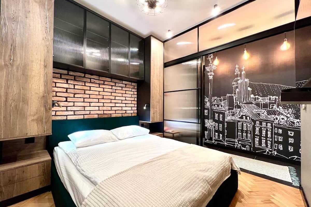 A modern bedroom with a brick accent wall, a large bed, and a cityscape mural.