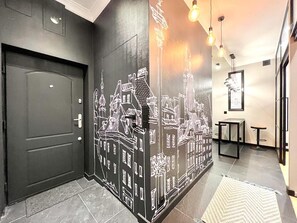 Un couloir avec une porte noire, un mur orné de plans architecturaux blancs et une petite table accompagnée de deux tabourets.