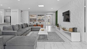A modern living room with a grey sectional sofa, a white coffee table, and a flat-screen TV mounted on a white wall. - 15BD Sonoma Resort Luxury House  (SR2609) (Kissimmee)