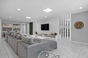 Un soggiorno moderno con un divano angolare grigio, una TV a schermo piatto montata a parete e un tavolino da caffè bianco.