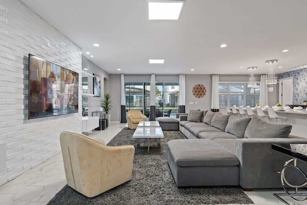 A modern living room with a sectional sofa, a coffee table, and a TV mounted on a white brick wall.