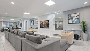 Ein modernes Wohnzimmer mit einem grauen Ecksofa, einem kleinen runden Tisch und einem weißen Kamin.