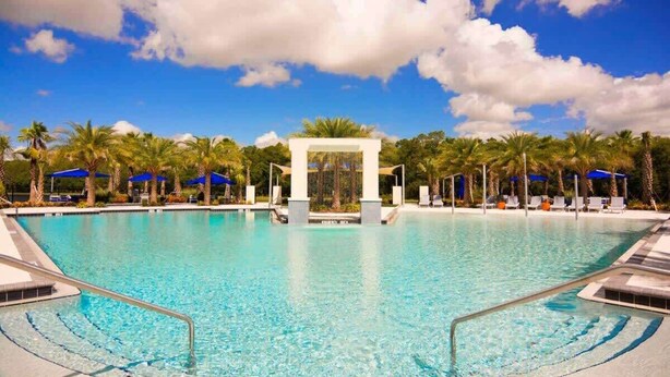 Una piscina trasparente con un arco centrale, circondata da palme e lettini da relax.