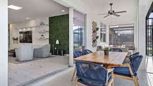 Un'area pranzo moderna con un tavolo in legno e sedie blu, una parete verde e una ventola a soffitto.
