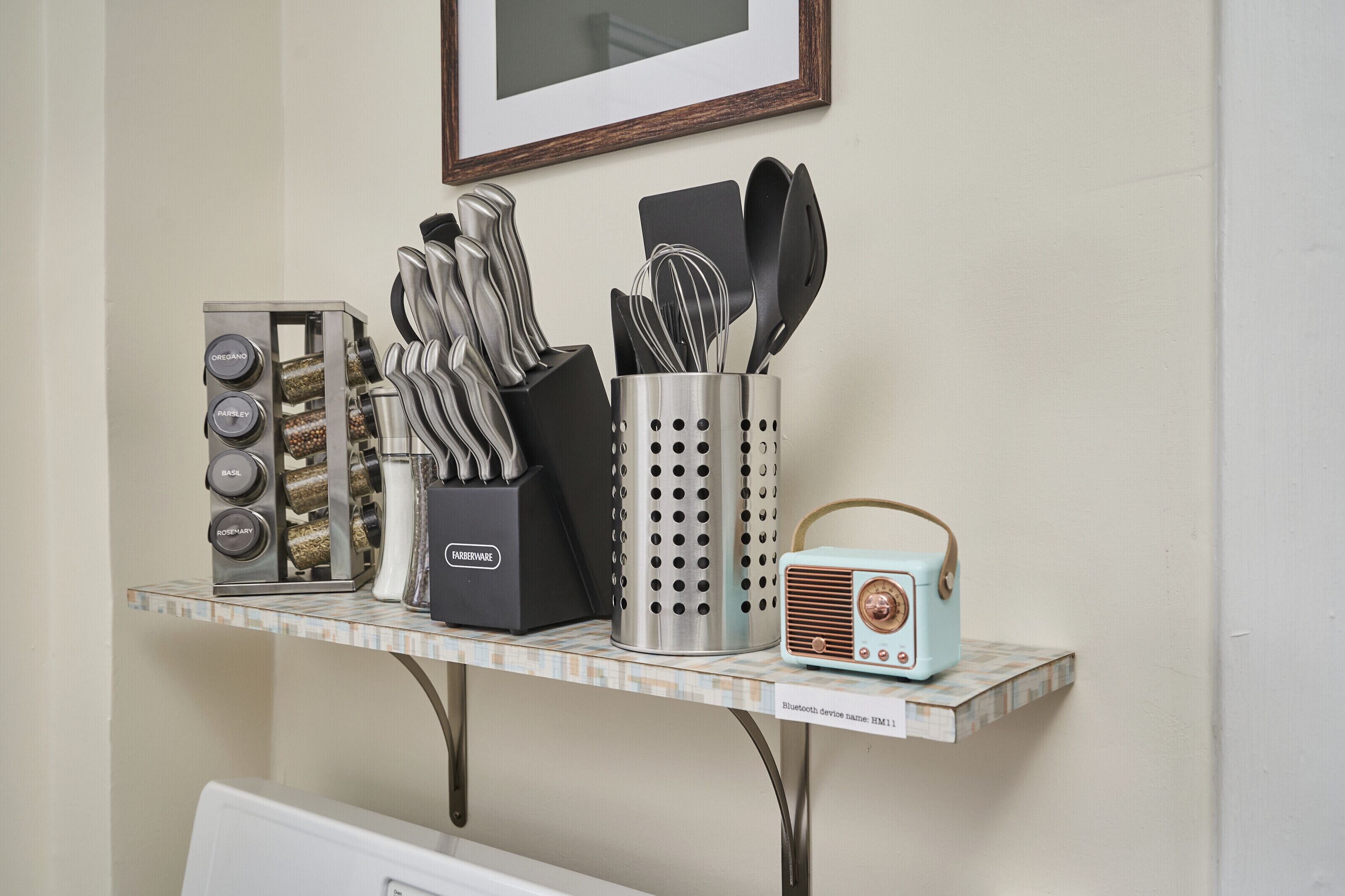 A kitchen counter with a food processor, a spice rack, a set of knives, a colander, and a vintage radio.