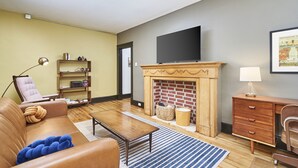 A living room with a leather sofa, a wooden coffee table, a fireplace, a television, and a bookshelf. - The Inn Too @ The Highland Hill (Akron)