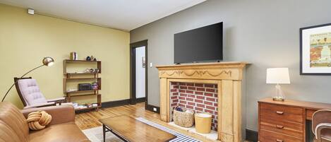 A living room with a leather sofa, a wooden coffee table, a fireplace, a television, and a bookshelf.