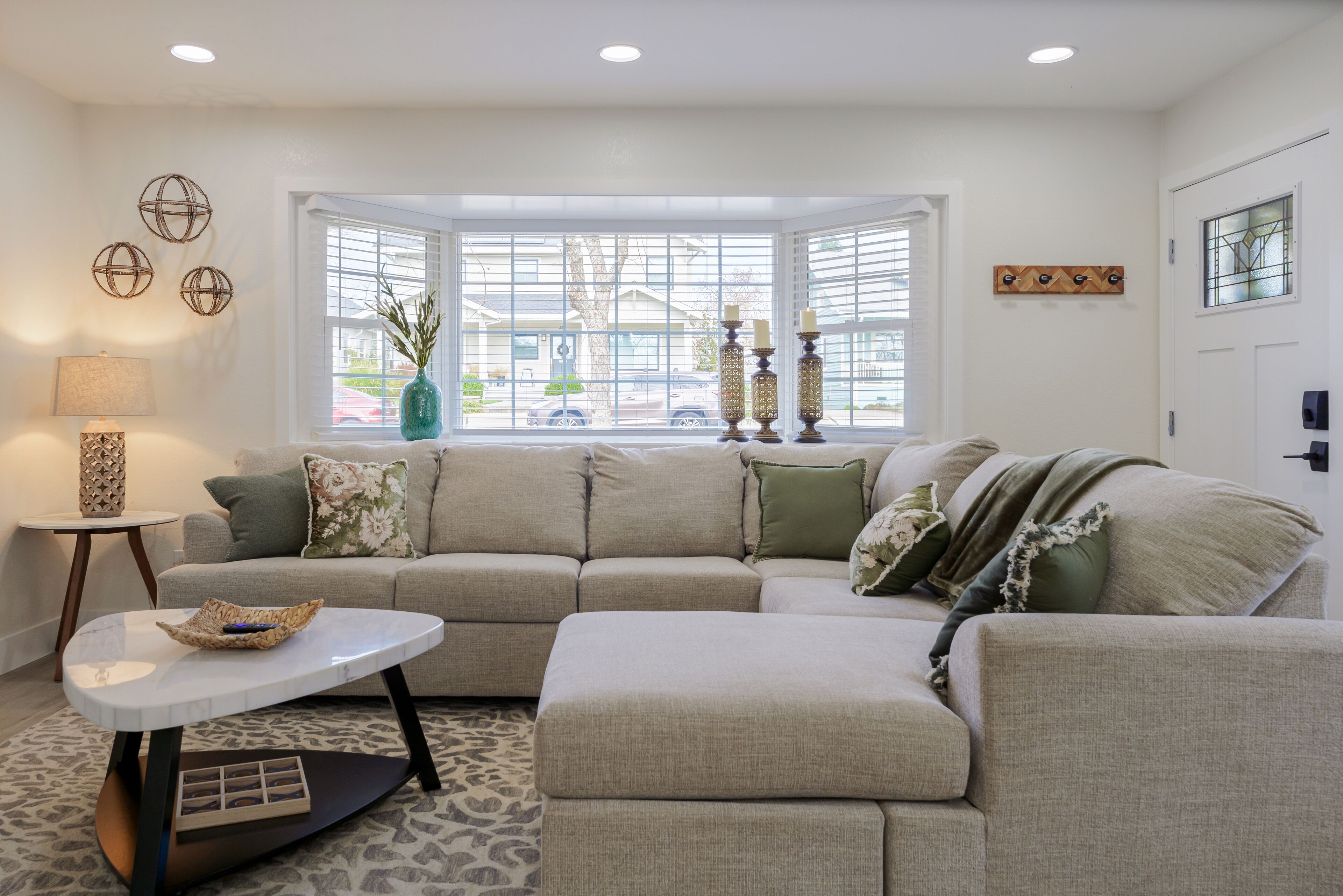 A modern living room with a sectional sofa, a round coffee table, and a bay window with decorative candles.