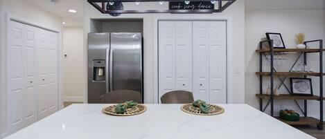 Una cocina moderna con encimera de mármol blanco, refrigerador de acero inoxidable y una lámpara colgante sobre la encimera.