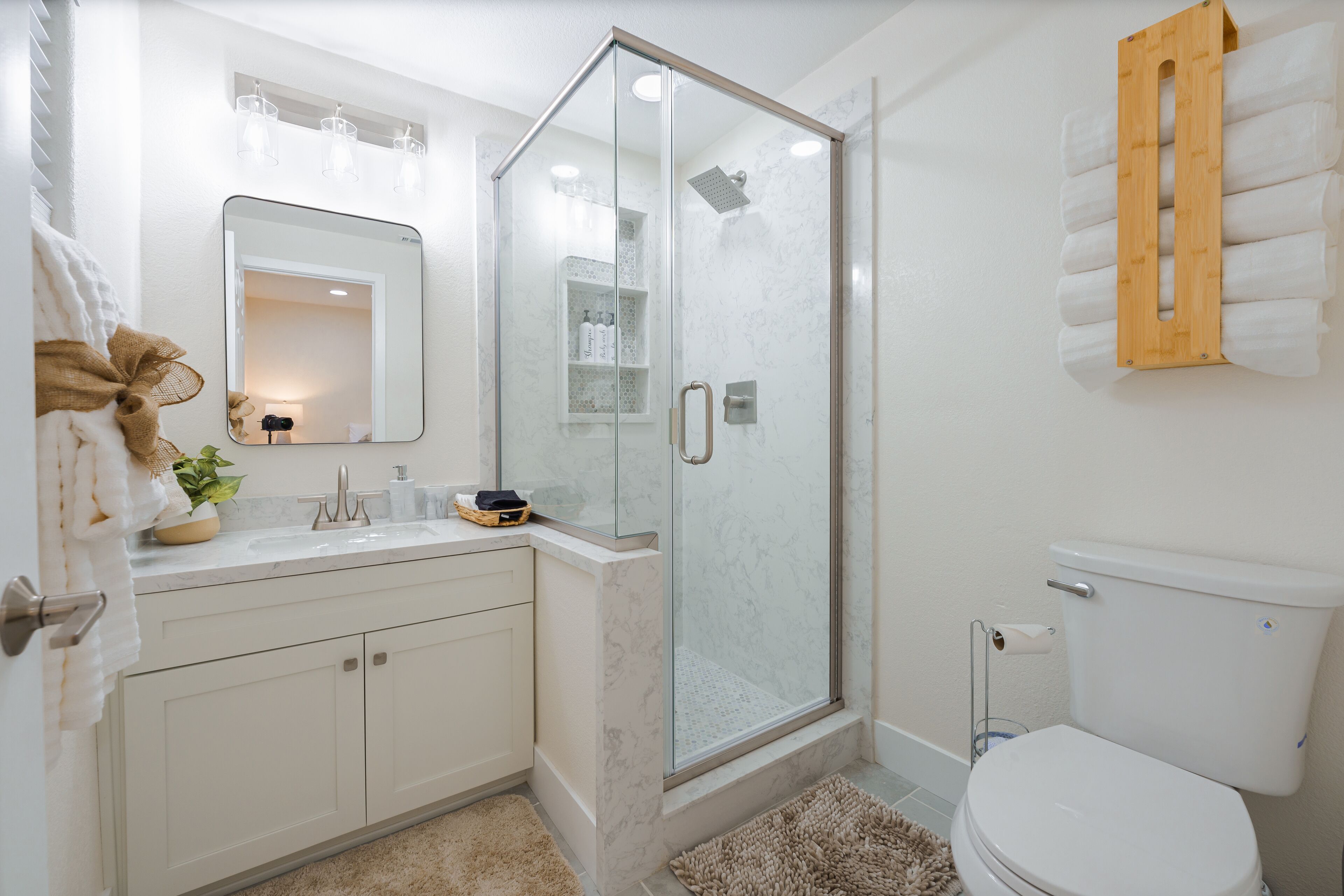 Une salle de bain moderne avec une douche à parois de verre, un lavabo blanc avec un miroir au-dessus et des toilettes dotées d’un porte-serviettes en bois.