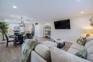A modern living room with a sofa, a dining table, and a TV mounted on the wall. - Historic Roseville Retreat with Hot Tub (Roseville)