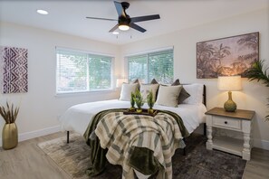 A bedroom with a bed, a ceiling fan, a nightstand with a lamp, and a window with blinds. - Historic Roseville Retreat with Hot Tub (Roseville)