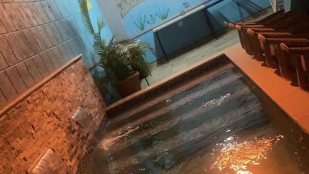 Un espace de détente avec un élément aquatique, des sièges en bois et une fresque murale.