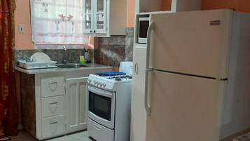 A kitchen with white cabinets, a stove, a refrigerator, and a window with curtains.