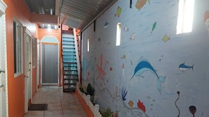 Un couloir doté d’un sol carrelé, d’une fresque murale représentant des poissons et des plantes marines, et d’un escalier menant à un niveau supérieur.