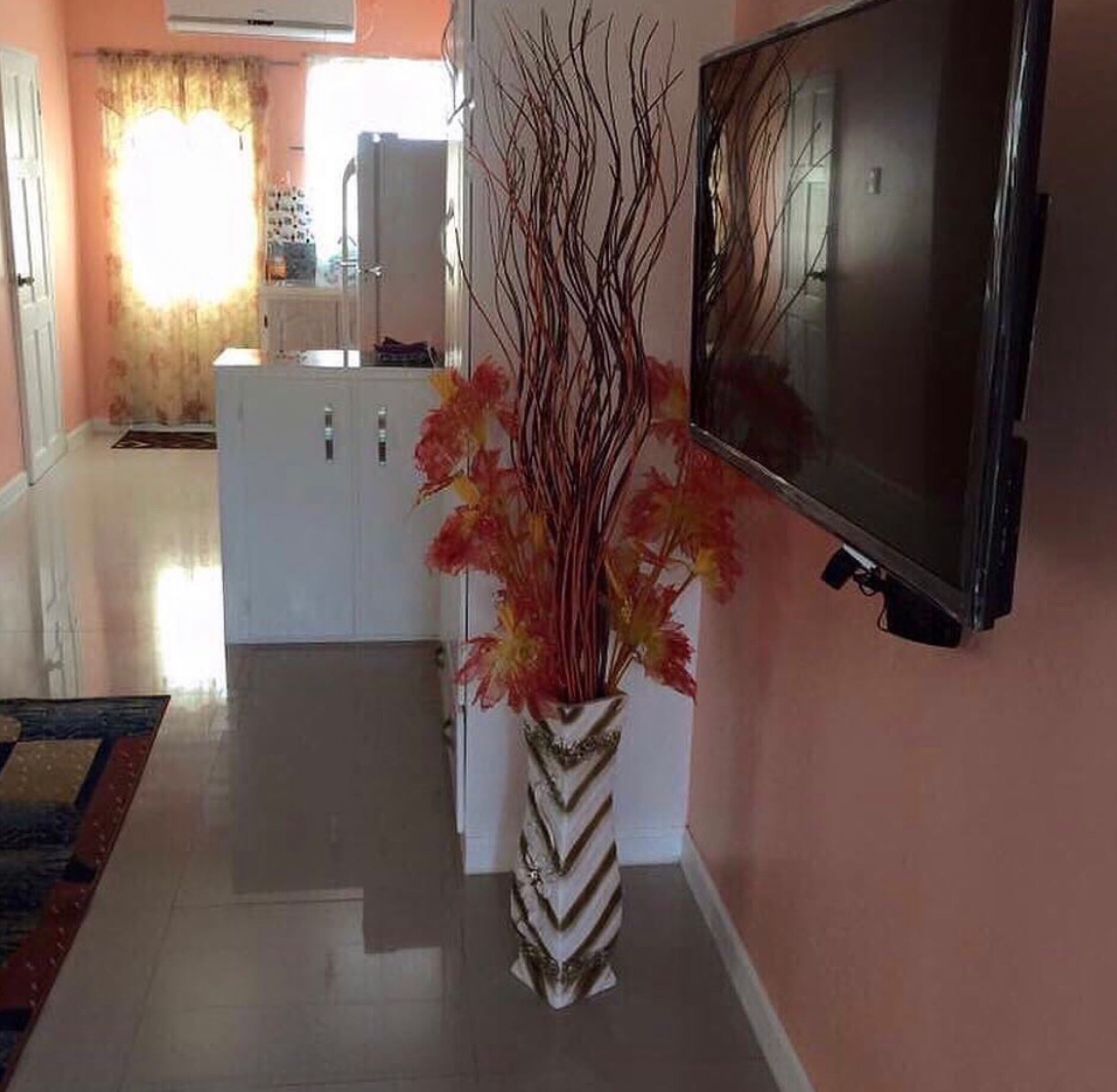 A modern living room with a flat-screen TV mounted on the wall, a white cabinet, and a decorative vase with branches.