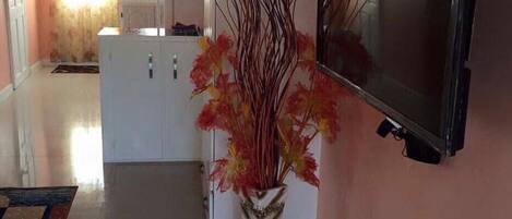 A modern living room with a flat-screen TV mounted on the wall, a white cabinet, and a decorative vase with branches.