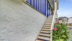 Un escalier en bois mène à une maison dont le mur est en briques blanches et le revêtement extérieur est bleu.