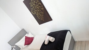 A neatly arranged bedroom with a bed, pillows, a bedside table with a lamp, a small plant, and a geometric wall art piece. - Room in Guest Room - Single Room in City Hotel in the Centre of Rastatt (Rastatt)