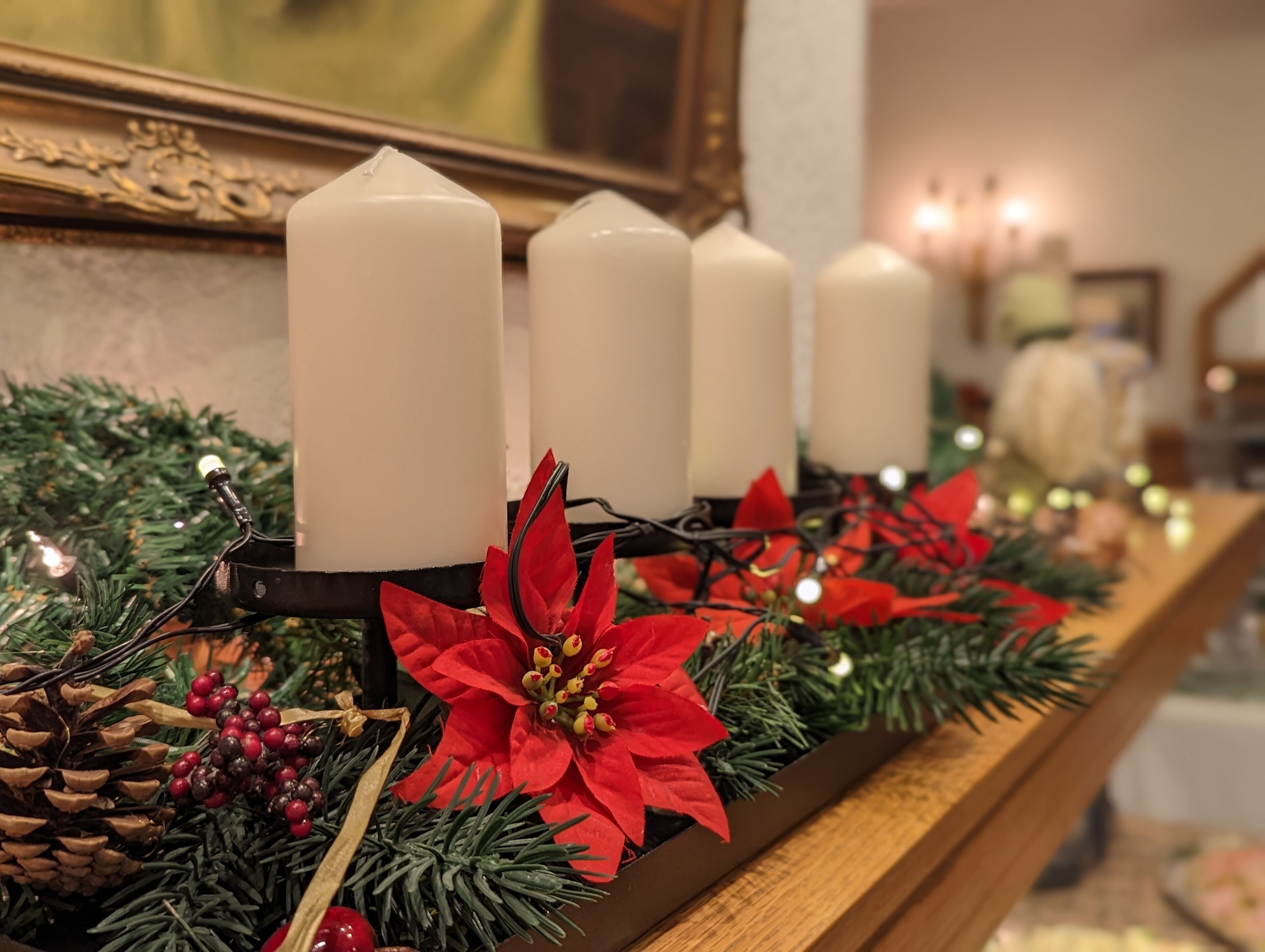 A row of white candles on a wooden surface, decorated with poinsettias and pine cones.