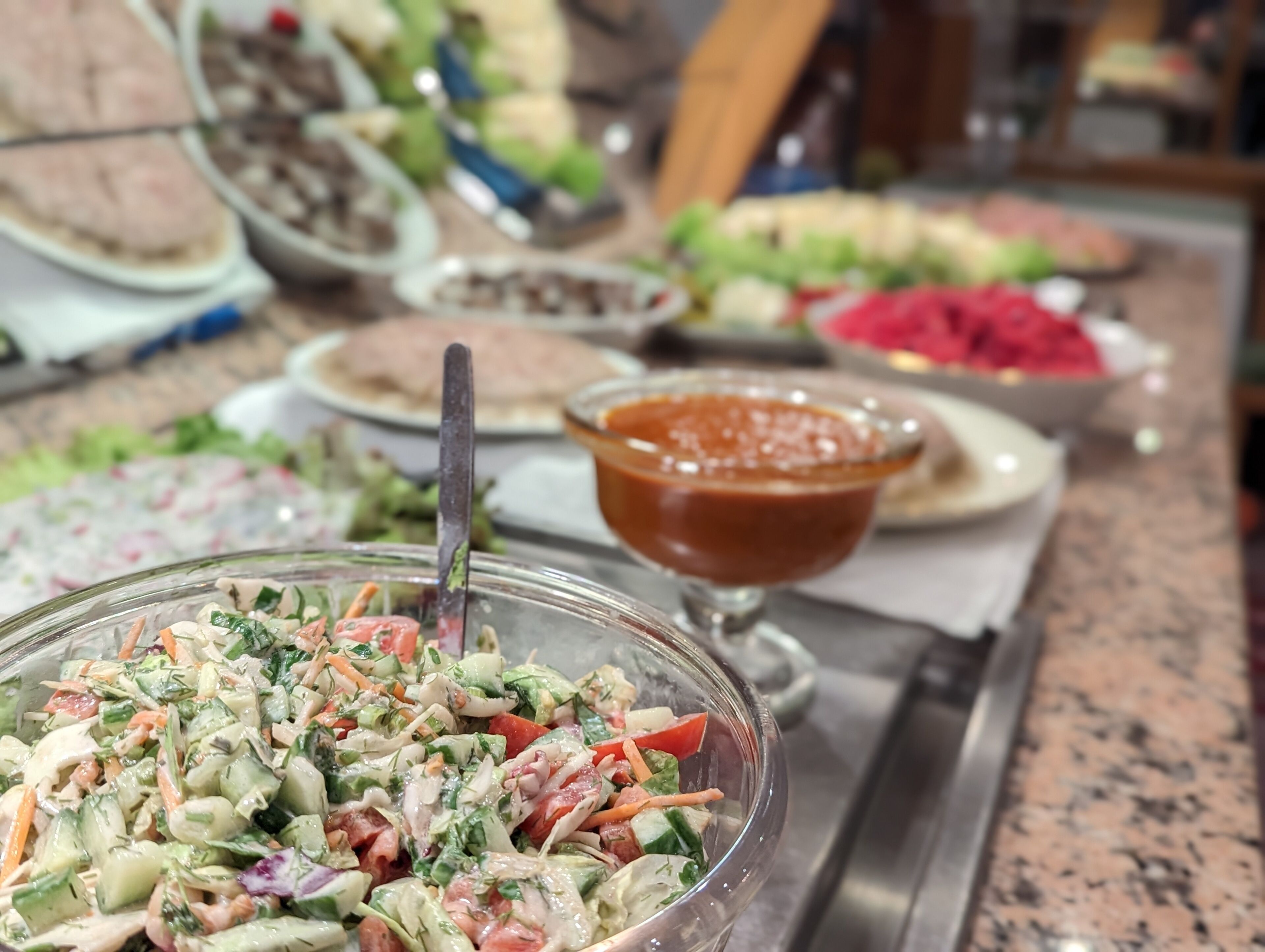 A buffet table with various dishes, including a salad, a bowl of sauce, and other food items.
