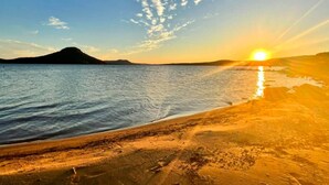 A beach with a sunset, calm water, and a distant mountain. - Greers Ferry Lake Life Dreams (Edgemont)