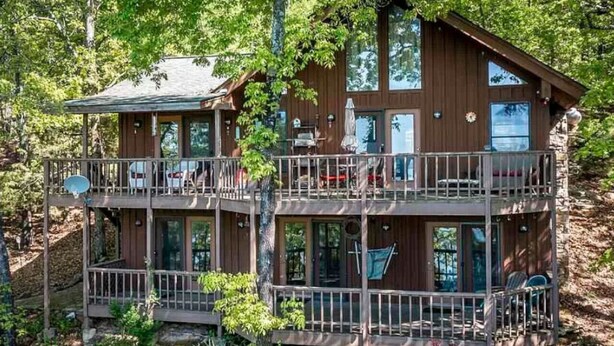 A two-story wooden cabin with balconies, large windows, and a satellite dish. - Greers Ferry Lake Life Dreams (Edgemont)