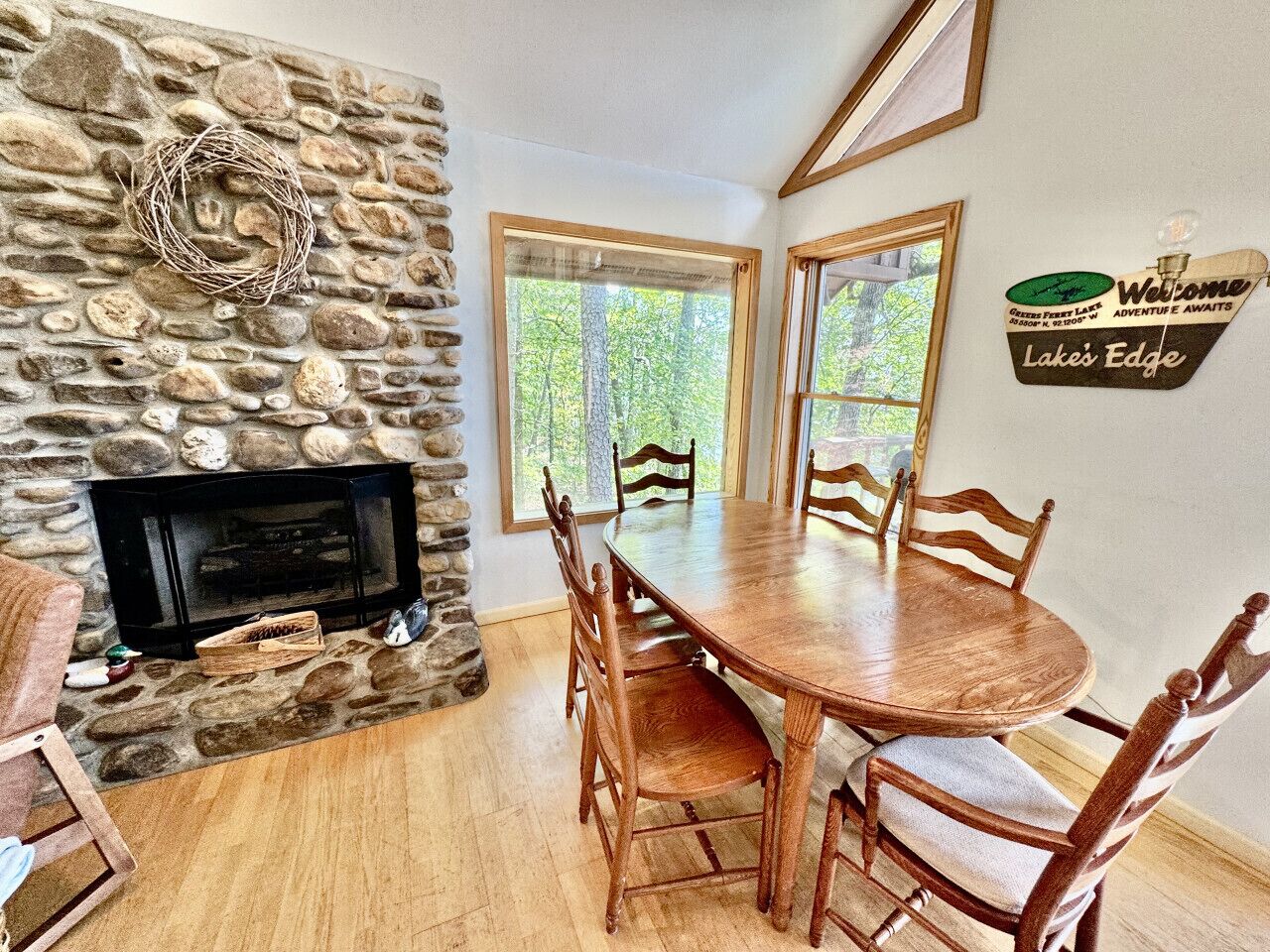 Une cheminée en pierre, une table de salle à manger ronde en bois avec des chaises, et une pancarte indiquant : « Bienvenue à Lake’s Edge ».