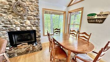 Une cheminée en pierre, une table de salle à manger ronde en bois avec des chaises, et une pancarte indiquant : « Bienvenue à Lake’s Edge ».