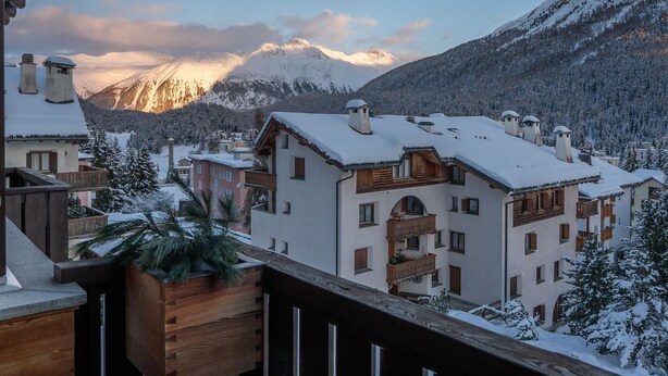 Un pueblo cubierto de nieve con edificios de estilo chalete, un balcón de madera y vistas a las montañas.